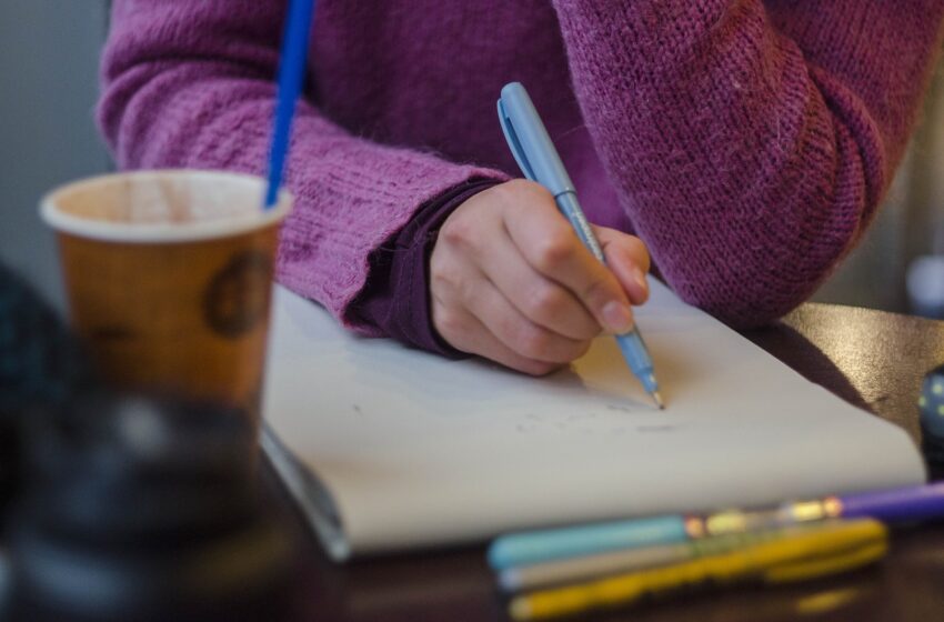 osoba w fioletowym swetrze z długopisem i notatnikiem