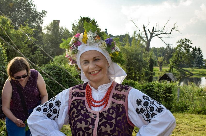 Kobieta w tradycyjnym urzeczańskim stroju w wianku na tle jeziora czerskiego i zamku w czersku