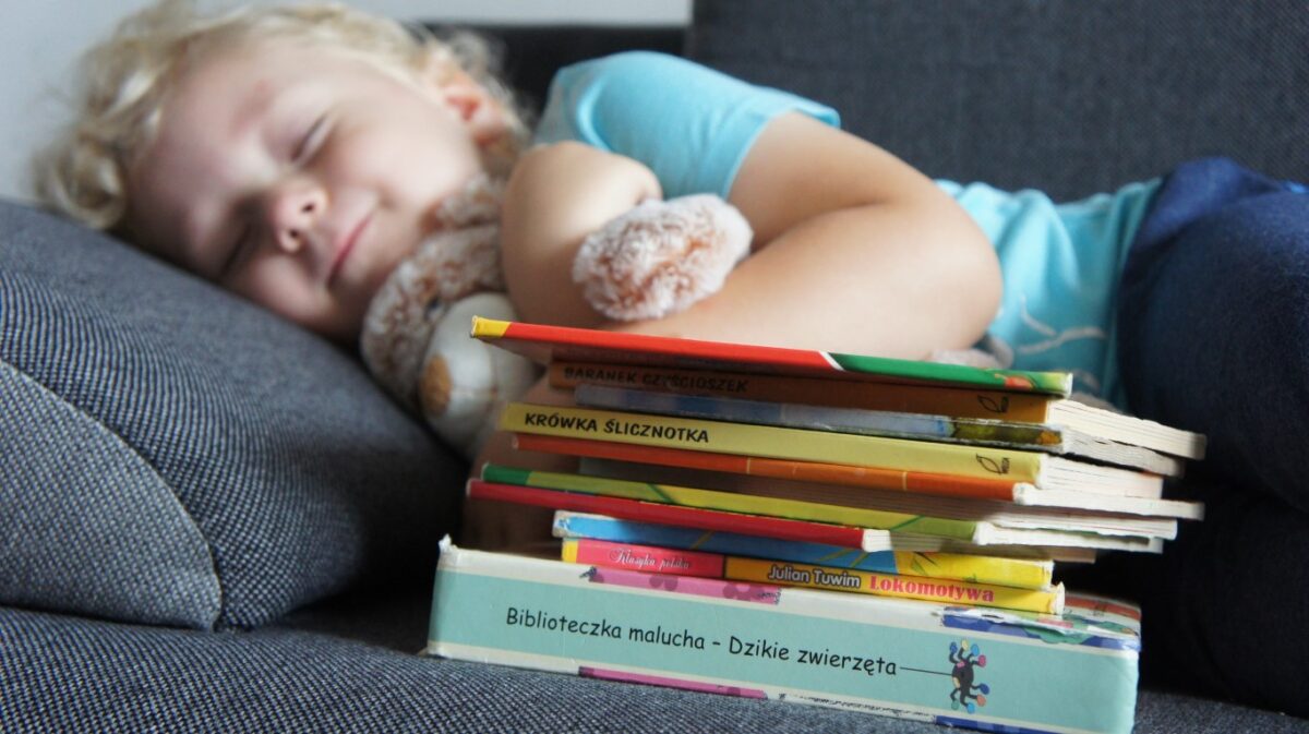 śpiąca dziewczynka na kanapie, przed nią książki