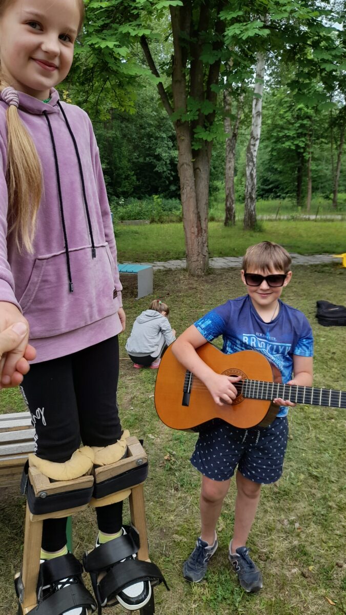 Dziewczynka na szczudłach i chłopiec grający na gitarze