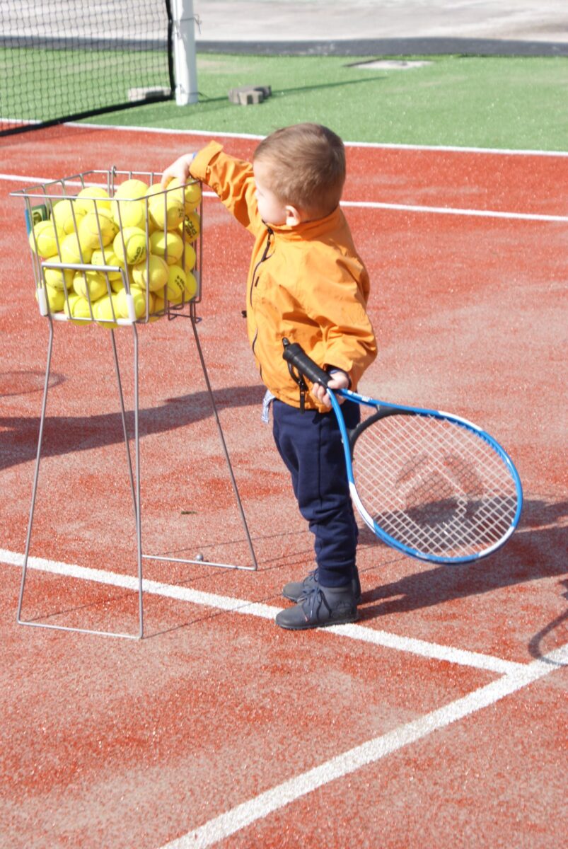 dziecko na korcie tenisowym trzyma rakietę i bierze piłkę z kosza