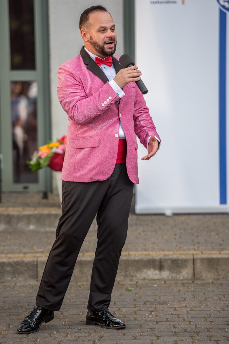 mężczyzna w różowej marynarce śpiewa