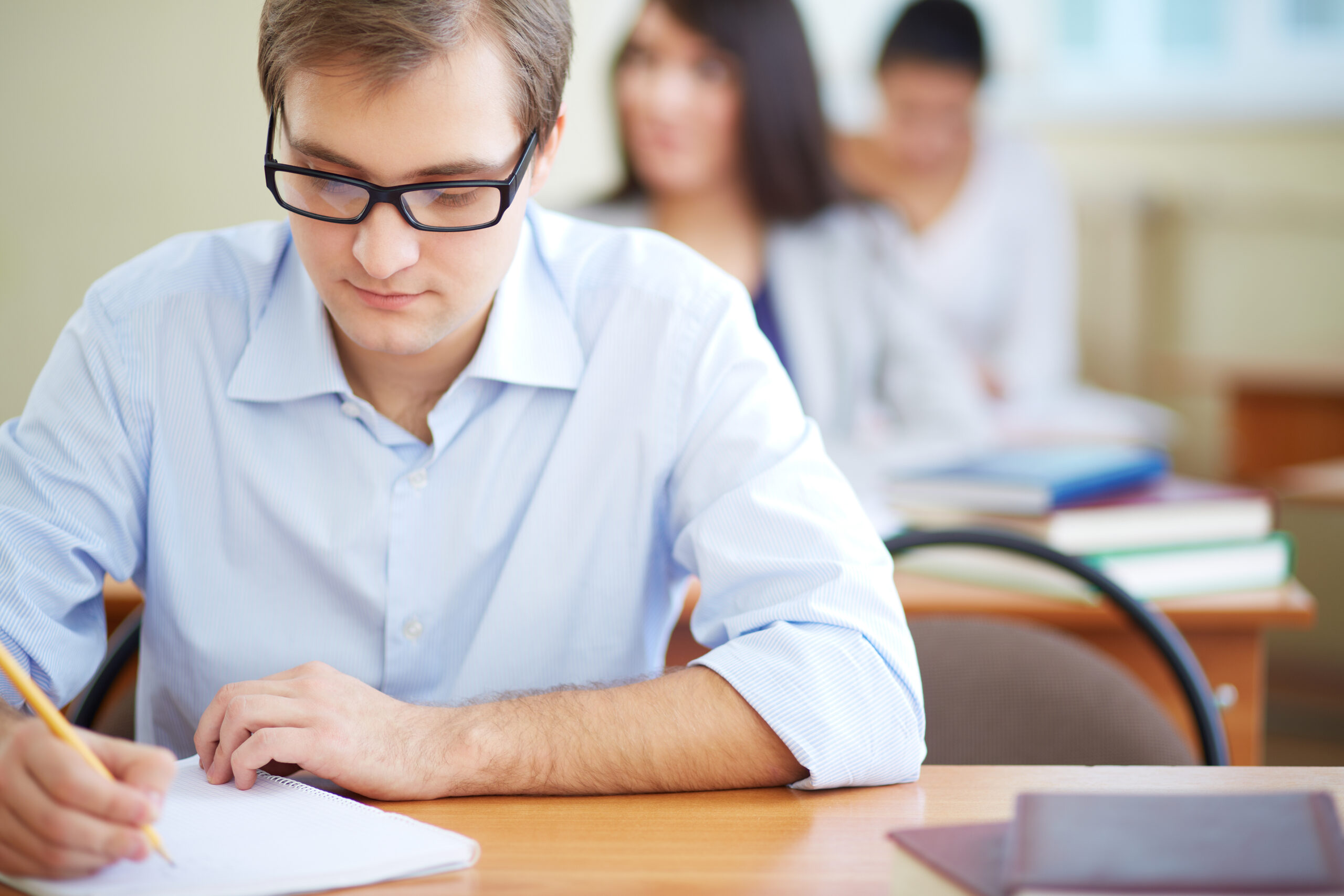 Portrait of group of students making notes or writing test with serious guy in front